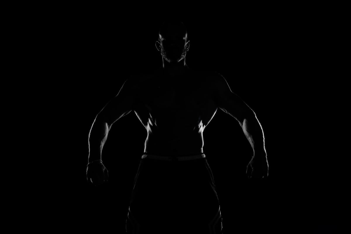Silueta de espalda y hombros masculinos musculados en contraluz sobre fondo oscuro — imagen editorial de banco