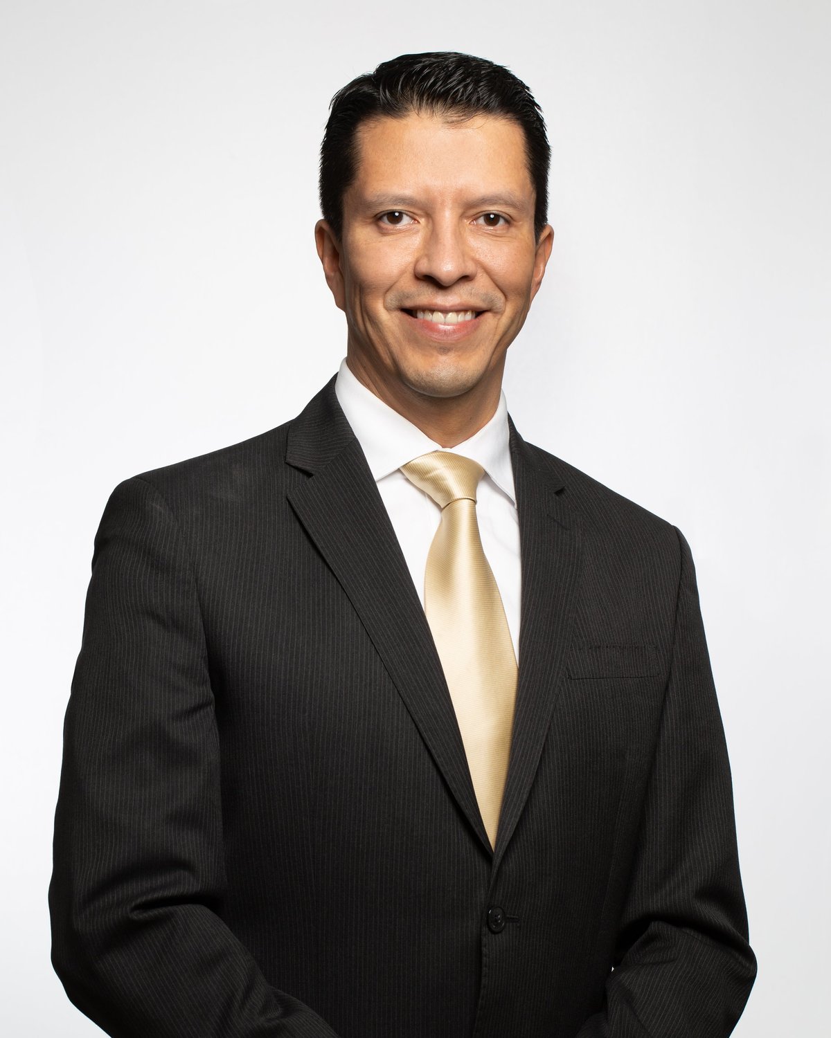 Retrato del Dr. Gabriel Mecott con traje oscuro de rayas, camisa blanca y corbata color champán, sonriendo sobre fondo blanco
